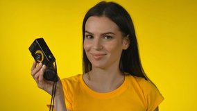 Cheerful woman is using a retro camera for shooting a picture in a yellow studio
