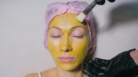 Procedure for skin care to face of young pretty woman. Beauty salon, facial peeling yellow gold alginate mask with retinol treatment, fruit acids.