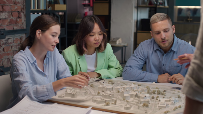 Architects and asian designer working on town area layout in modern office. Diverse group of creative people at table talking and discussing houses design. Co-workers look at model projection of homes Royalty-Free Stock Footage #1081232546