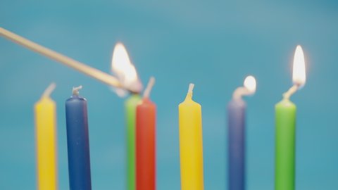 Colorful birthday candels light up with a match isolated on blue background shot in 4k super slow motion