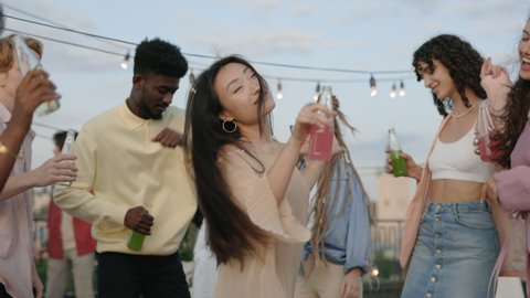 Charming asian woman having fun with mixed race friends on rooftop party. Group of carefree young people dancing with drinks in hands. Relaxation and enjoyment concept. Video stock