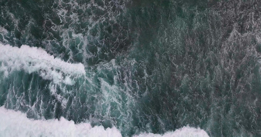 Spining Overhead shot of The waves crashing in the ocean with sea water that looks bluish and produce white foam. Watu Kodok Beach, Indonesia Royalty-Free Stock Footage #1081233347