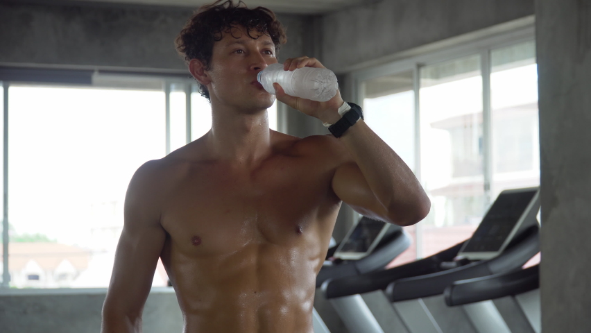 Handsome muscular man running  on treadmill finished exercise drinking water in fitness gym . Shirtless sport guy workout  on running Machine . bodybuilder cardio training