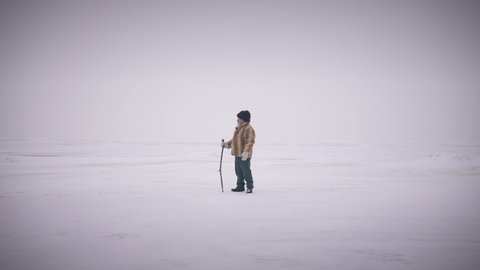 Extreme wide shot happy confident senior adventurer standing on white picturesque polar landscape looking around. Old indigenous man outdoors on cold winter day. Scenics and lifestyle