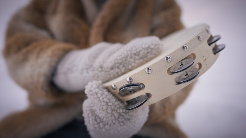 Close-up tambourine in male hands in mittens drumming in slow motion. Unrecognizable old indigenous man playing folk music on percussion instrument outdoors on icy snowy winter day Royalty-Free Stock Footage #1081237115