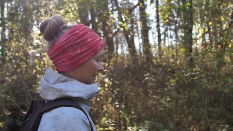 Buff a woman with tied hair on her head. A beautiful white woman with a headscarf was walking in the autumn forest at sunset. Sun shines on a woman on top of a forest walk. Beautiful woman with a he.