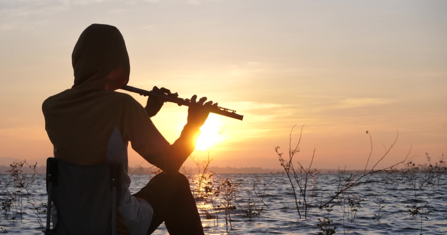 silhouette male musician with flute, lake during beautiful sunrise, landscape of camping