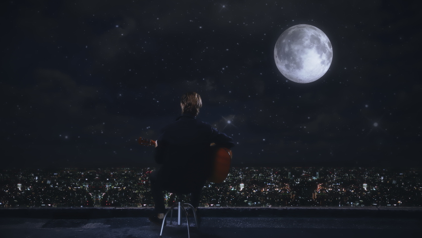 Playing Music Under Moonlight Over City at Night, Man Playing Guitar Alone. Male musician playing acoustic guitar under moonlight on top of a building with city view at night