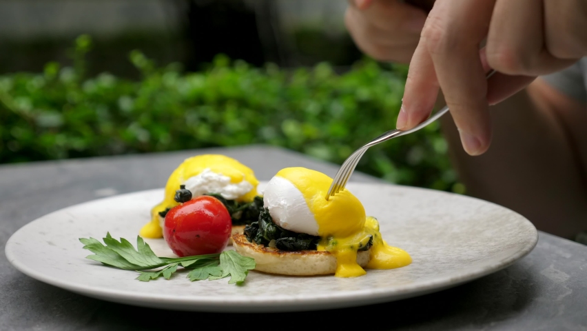 Healthy morning food. Man eating delicious poached eggs at breakfast in hotel. Male hands cuts egg Benedict with liquid egg yolk inside, hollandaise sauce and spinach on english muffin. Close up Royalty-Free Stock Footage #1081254497