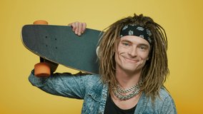 Portrait stylish hipster man holding skateboard on shoulder in studio. Closeup smiling skateboarder posing on yellow background. Positive young guy millennial looking camera with longboard.  - Powered by Shutterstock - Get 15% off with code: PIKWIZARD15