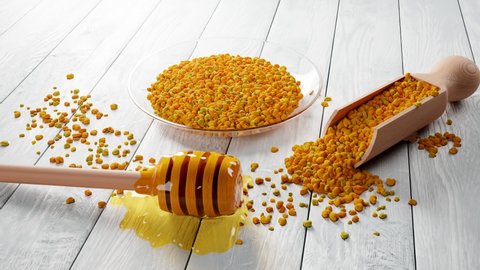 A composition with honey dipper, wooden scoop and glass bowl full of yellow bee pollen granules. Heap of flower pollen. Useful and valuable beekeeping products. Natural healthy supplement. Superfood.