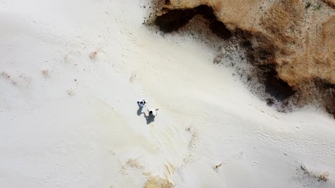 A romantic couple runs along the white sand in a beautiful canyon in the middle of nature. Aerial shot of people running through an edged of a sand dune in a desert
