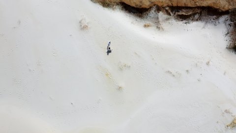 A romantic couple walk on white sand in a beautiful red canyon in the middle of nature. Aerial shot of people resting along the edge of a sand dune in the desert
