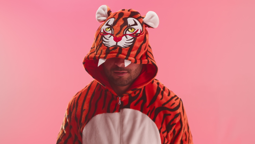 Man wearing tiger costume showing roars on red background. Symbol of 2022 year. Male model in kigurumi pajamas looking in camera. Young guy in funny clothes. Chinese zodiac, calendar sign. Royalty-Free Stock Footage #1081264997