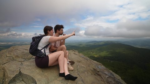 Young couple sitting on a rock high above Virginia pointing in the direction of Charlottesville.