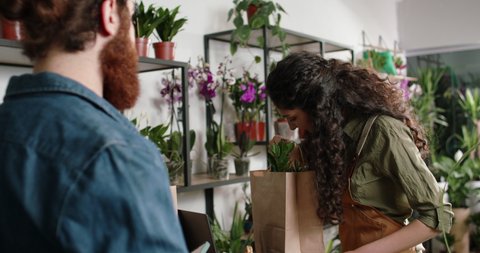Customer paying for purchase in flower shop using nfc mobile technology. Asian female entrepreneur positively smiling - small business 4k footage