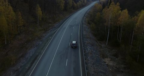 One gray silver crossover SUV car driving alone road trip, travel on freeway through dense colorful forest corridor at autumn sunny sunset - Aerial drone wide view