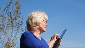 Mature middle aged adult woman holding digital tablet computer outdoors
