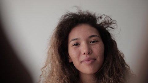 Smiling woman with curly hair and freckles on her face takes pictures of herself.
