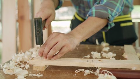 Asian man who owns a small  business is process wood for renovate House. A carpenter is using a hammer to drive nails to hold the wood together. home renovate concept.
