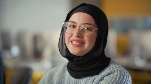 Beautiful Portrait of a Multiethnic Muslim Female Wearing Hijab and Glasses, Charmingly Smiling and Posing on Camera. Happy Diverse Young Woman in Casual Clothes Indoors.