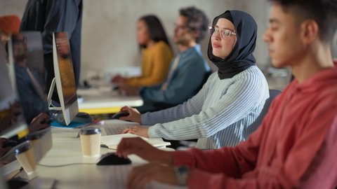 Curious Female Muslim Student Wearing a Hijab, Studying in Modern University with Diverse Multiethnic Classmates. College Scholars Work in College Room, Learning IT, Programming or Computer Science.
