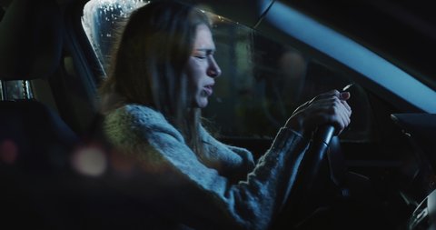 Cinematic shot of frustrated angry woman is screaming in anger, gesturing with hands and shouting alone on driver's seat of her car after traffic violation accident while while waiting car assistance.