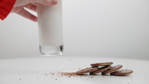Hand putting glass with milk as chocolate powder falling in liquid to cookies on table. Unrecognizable young Caucasian woman preparing sweet delicious breakfast close-up