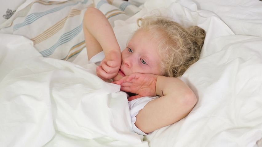 Cute little girl with blond hair coughs and sneezes in bed, five-year-old girl got sick | Shutterstock HD Video #1081286345
