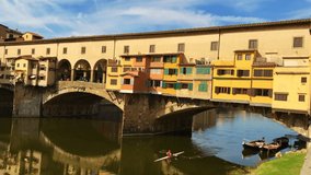 View of the Ponte Vecchio - Old Bridge - in Florence (Firenze), Italy - by the river Arno with reflections in the water and blue sky. Famous landmark in Tuscany. Panning shot video.