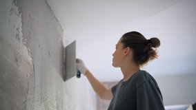 A professional repairwoman puts a plaster on the wall with a spatula. Female repairing the wall with a putty knife. The internal construction and finishing work. Young woman doing home repairs. - Powered by Shutterstock - Get 15% off with code: PIKWIZARD15