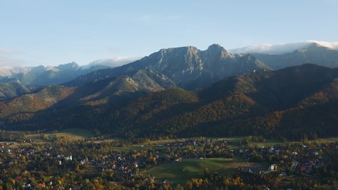 Aerial view flight over alpine village lit with evening sunlight. Drone shot beautiful highland valley in sunset light. Picturesque Tatras mountains range covered with clouds, Poland, Zakopane