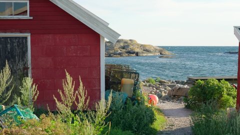 Swedish fishing house cabin or shed in red with crab lobster traps stocked. Zoomed in cinematic view between building towards ocean at Skagerrak bay. Landscape nature slow motion shot