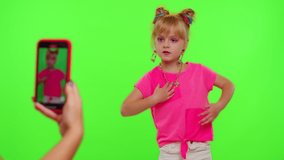 Happy little Caucasian kid girl blogger front of phone camera record video enjoy dance content on green chroma key background. Social distance coronavirus pandemic concept. Freedom active lifestyle