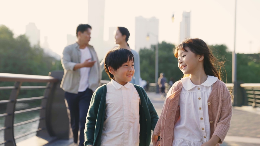 Two happy asian children walking in park with parents in background