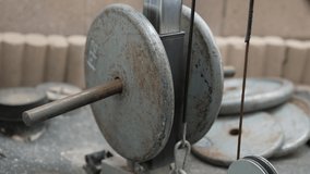 This close up video shows weights on a cable pull down machine going up and down at an industrial, old and beat up outdoor gym setting.