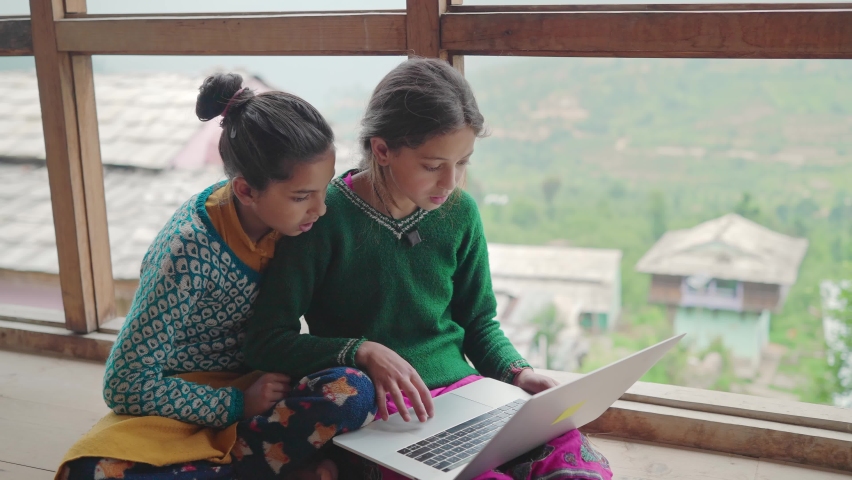 Two young village or rural school girls sitting indoors and using the laptop with the internet to study in an interior house with the green mountains in the back. learning and female education concept Royalty-Free Stock Footage #1081305077