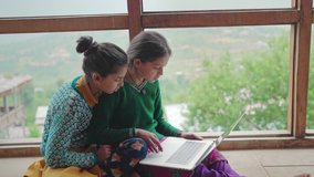 Two young village or rural school girls sitting indoors and using the laptop with the internet to study in an interior house with the green mountains in the back. learning and female education concept - Powered by Shutterstock - Get 15% off with code: PIKWIZARD15