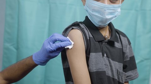 Maski, India - October 26, 2021 : Doctor pasting sinovac bandage after kid with medical face mask getting vaccine shot, Coronavirus or covid vaccination for children from china