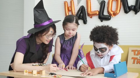 Young mother daughter and son in witch and vampire costume face painting are drawing vampire cartoon in halloween party.