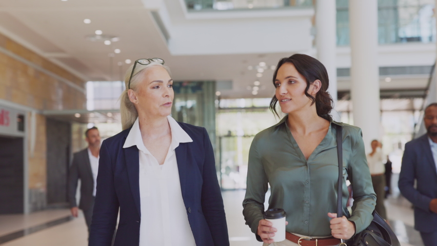 Two business women walking and talking in office. Two successful women manager discussing work while entering office building. Mature business woman talking with her assistant while going to work.
