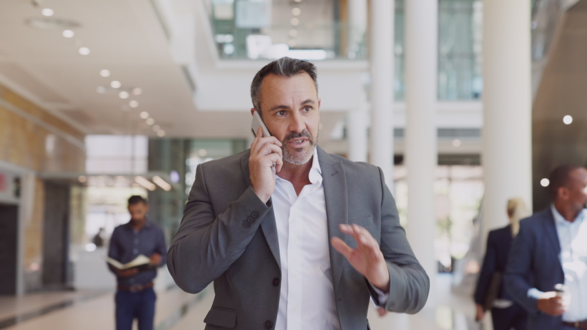 Business mature man walking while talking over smartphone at airport. Successful businessman in business centre doing a conversation on the phone. Happy mid adult man talking over mobile phone. | Shutterstock HD Video #1081307813