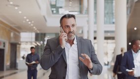 Business mature man walking while talking over smartphone at airport. Successful businessman in business centre doing a conversation on the phone. Happy mid adult man talking over mobile phone. - Powered by Shutterstock - Get 15% off with code: PIKWIZARD15