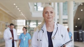 Portrait of mature female doctor walking on hospital corridor. Confident general practitioner walking in hospital hallway with her healthcare team in background. Successful head physician at clinic. - Powered by Shutterstock - Get 15% off with code: PIKWIZARD15