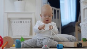 Baby sitting on the floor exploring new world around him touches everything, cute 7 month old baby boy playing with toys at home. High quality 4k footage
