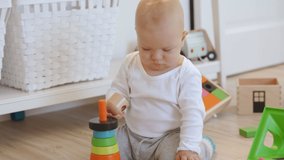 Baby sitting on the floor playing with toys, cute little baby boy having fun playing with wooden multicolor stacking rings. High quality 4k footage