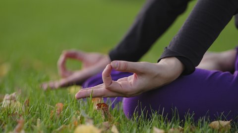 Woman girl doing morning practice in city park nature green grass lawn. Detail shot female fingers hands sitting in lotus pose meditates doing spiritual practices lessons meditation yoga exercises