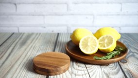 Video clip female hand serving a glass of sparkling lemon iced tea or iced tea with carbonated water decorated with fresh sliced lemon and rosemary branch on wood planks table and white brick wall.
