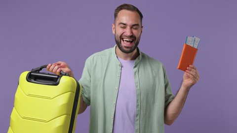 Traveller tourist young bearded man 20s wear mint shirt hold in hand globe choose place country take passport boarding tickets suitcase bag go isolated on plain light purple background studio portrait