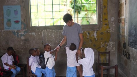 Zanzibar , Tanzania - 07 28 2021: African kids playing and hugging a white volunteer.